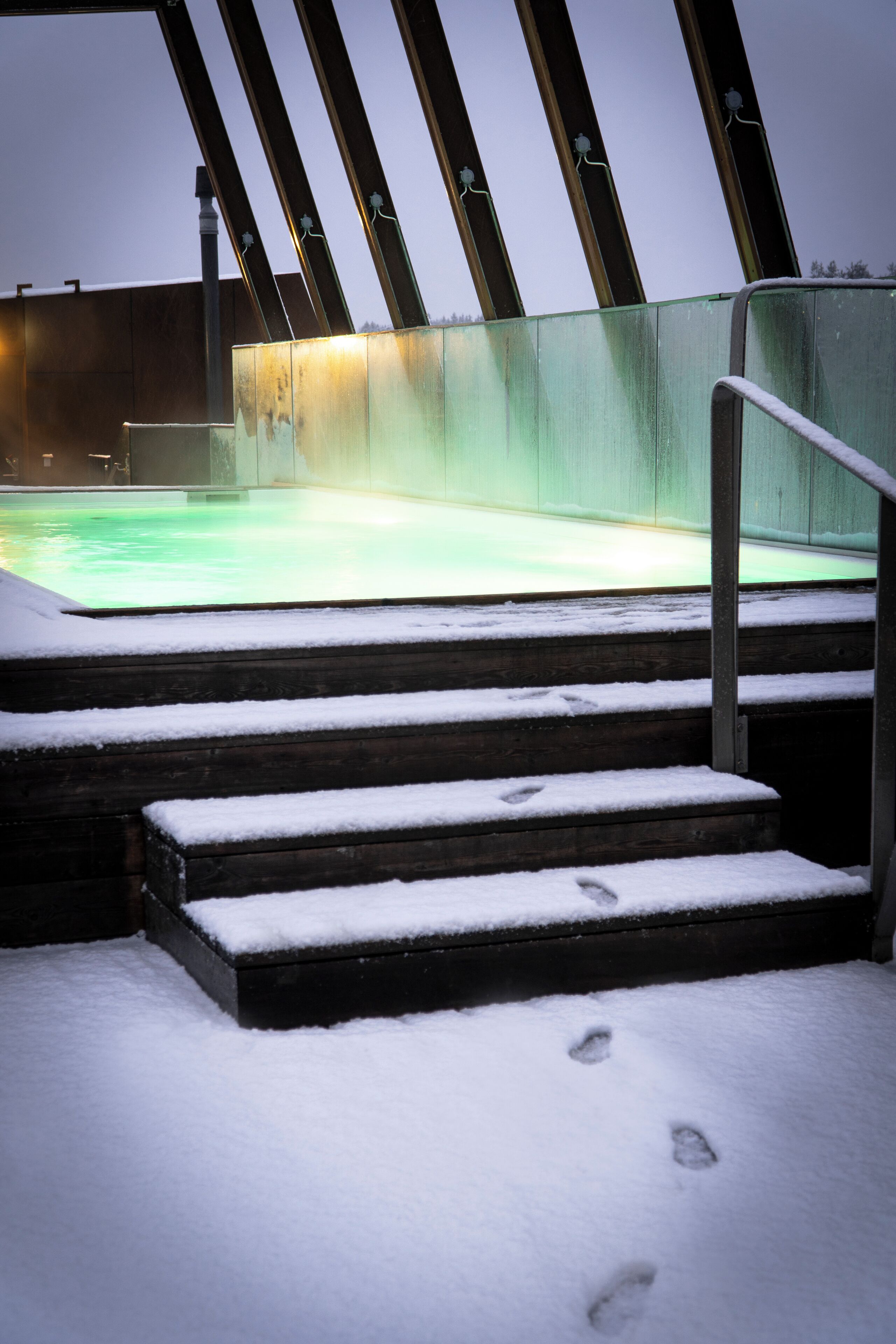 Ett snötäckt utomhusområde med en pool, trappsteg som leder upp till poolen och ett metallräcke.