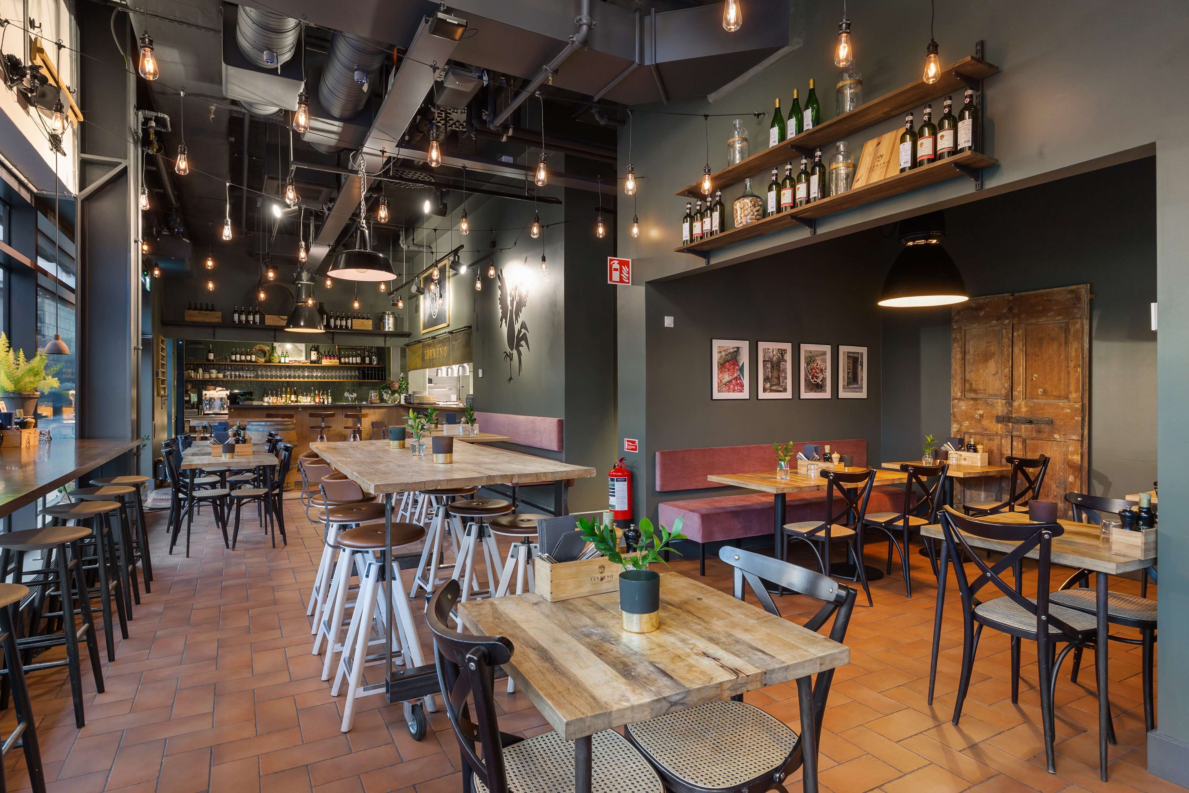 Un restaurante con mesas y sillas de madera, una zona de bar y estanterías llenas de botellas.