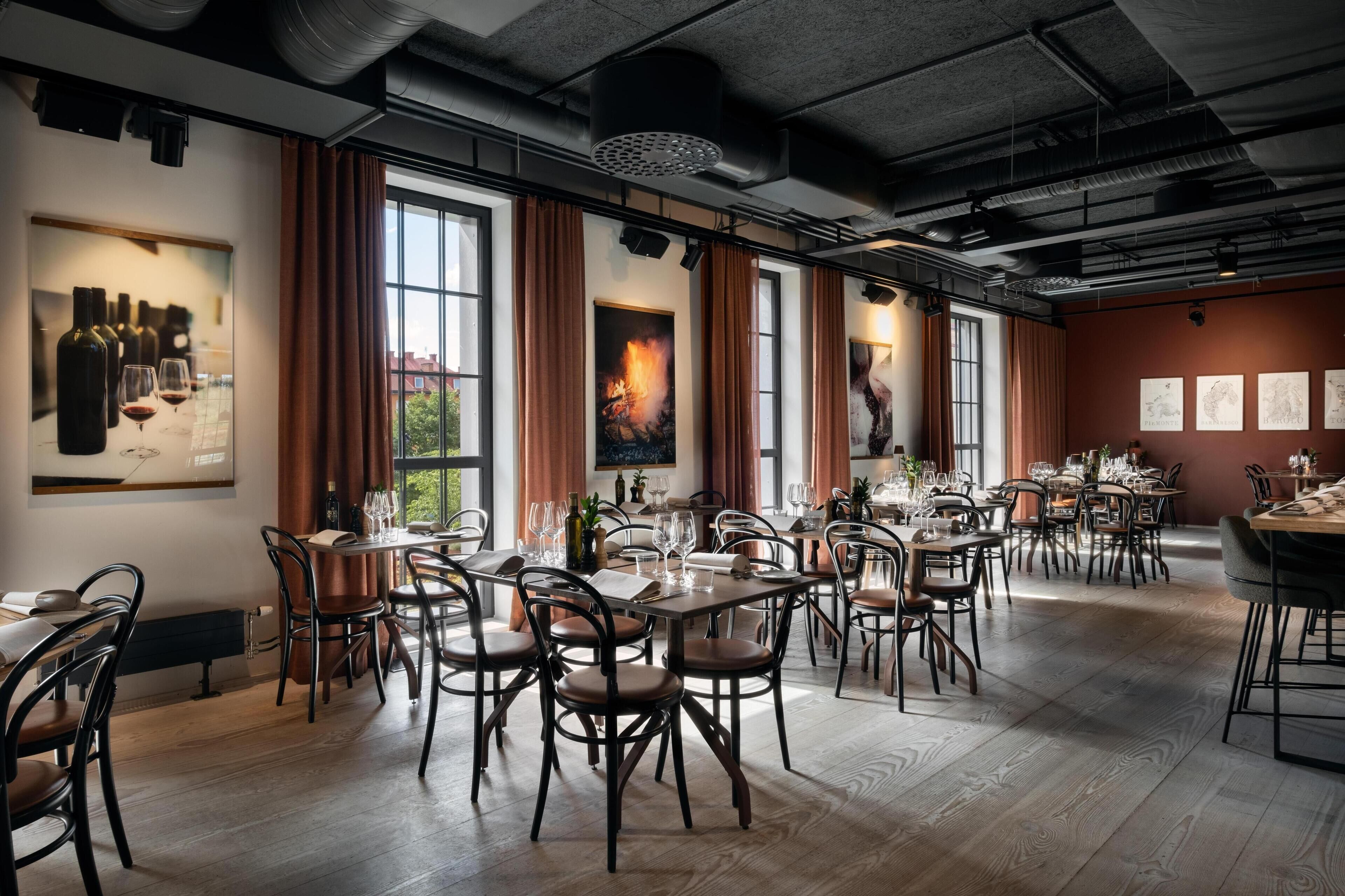Un comedor espacioso con varias mesas y sillas, ventanas amplias con cortinas y obras de arte en las paredes.