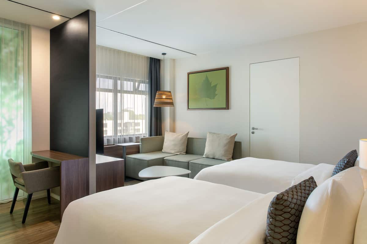 A hotel room with two beds, a desk, a sofa, and a chair.