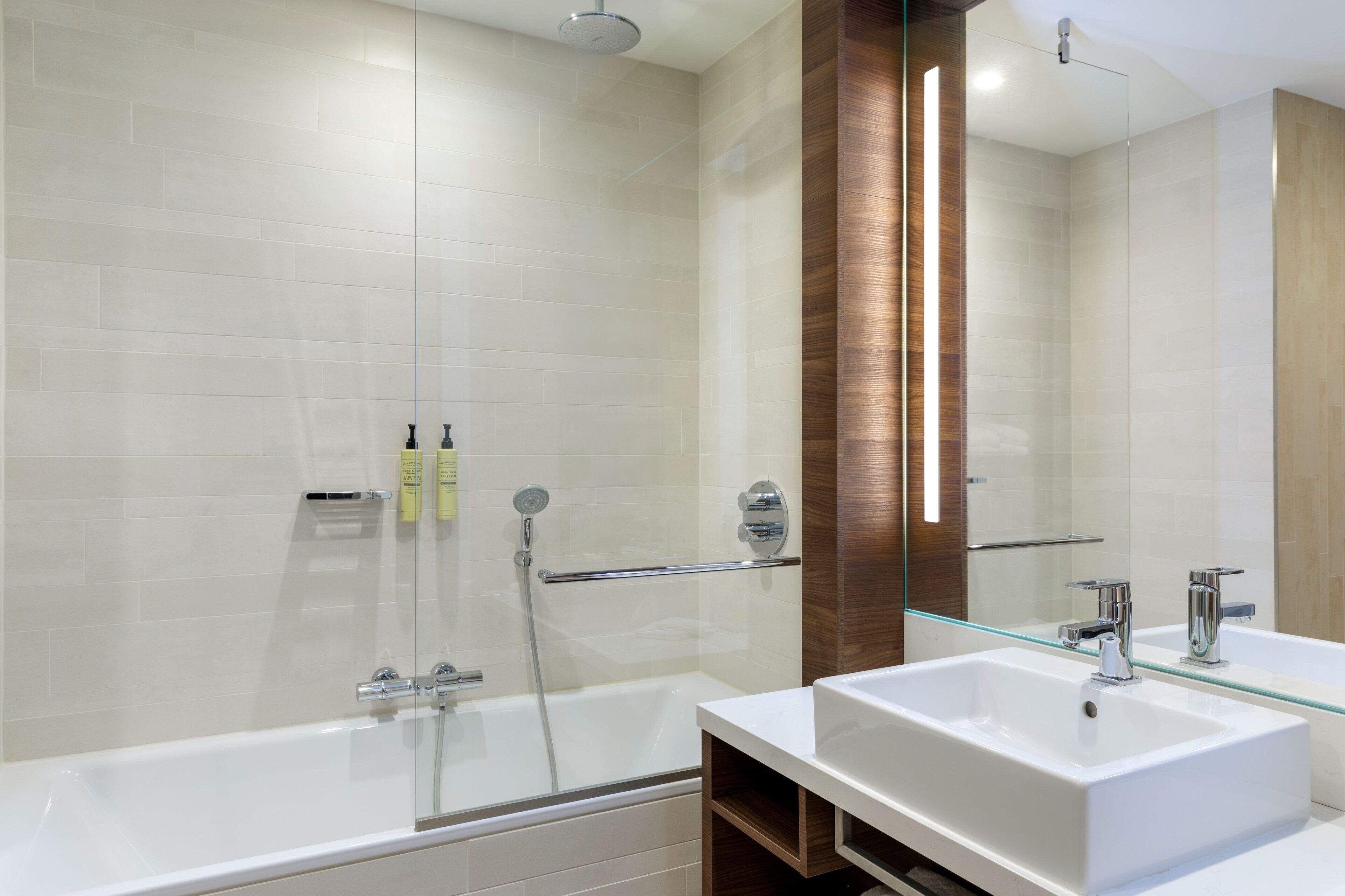 Un baño moderno con cabina de ducha de vidrio, un lavabo blanco y un espejo grande.