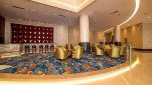 Een ruime lobby met een hoge plafond, een kamerbreed tapijt en een zithoek met gouden stoelen.