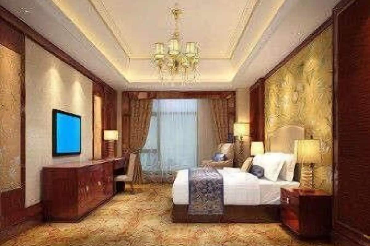 A hotel room with a large bed, a TV, a desk, and a chandelier.
