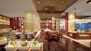 Een ruime hotellobby met een centraal gelegen eetgedeelte, diverse zithoeken en een uitzicht op de stad door grote ramen.