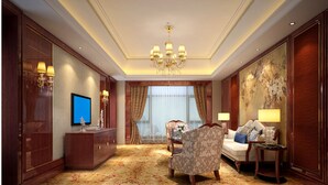 Ruime hotelkamer met een groot flatscreen televisietoestel, een kroonluchter, een bank, een stoel en een tafeltje met een lamp.