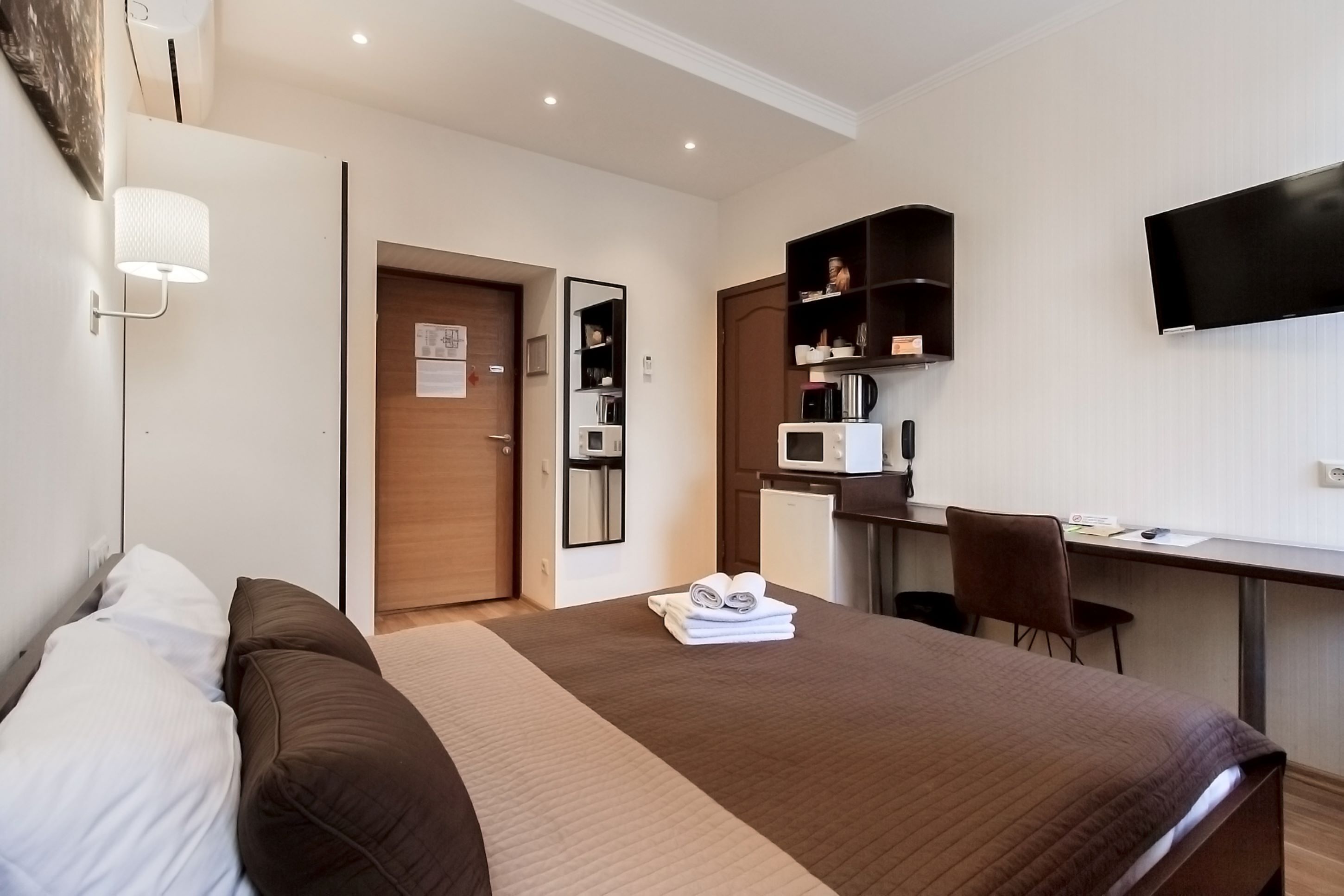 A hotel room with a bed, a desk, a microwave, a television, and a wardrobe.