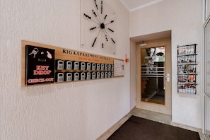 A hallway with a key drop check-out sign, a self-check-in kiosk, and a door leading to a room with a glass door and a shelf with items.