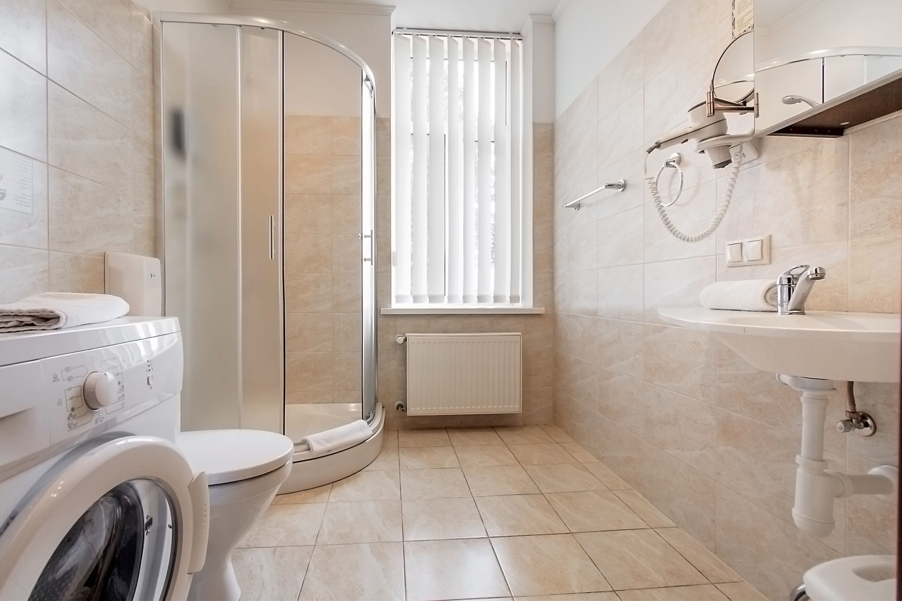 A modern bathroom with a glass-enclosed shower, a toilet, a washing machine, and a sink.