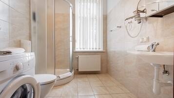 A modern bathroom with a glass-enclosed shower, a toilet, a washing machine, and a sink.