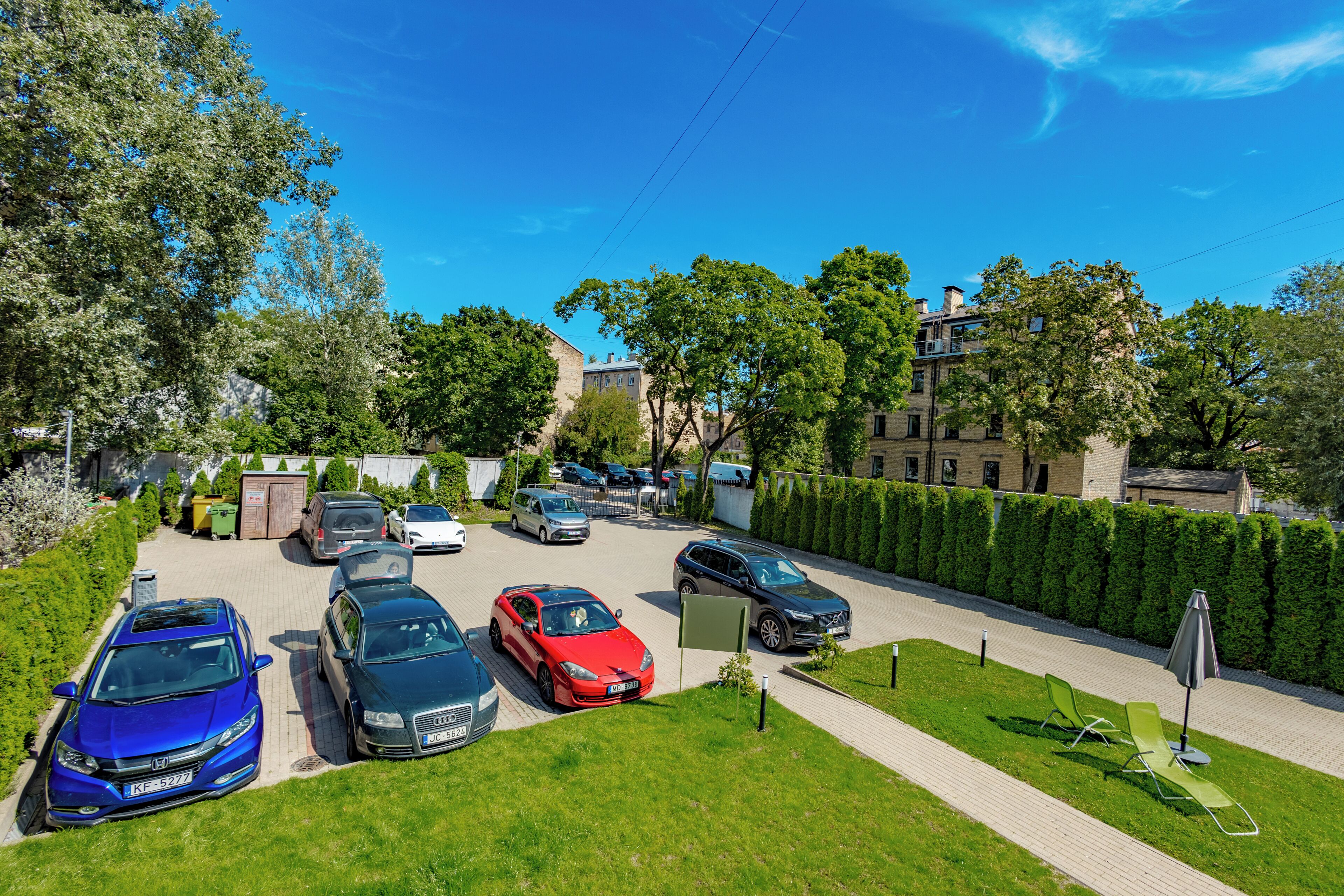 A parking lot with multiple cars, a green lawn, and a hedge.