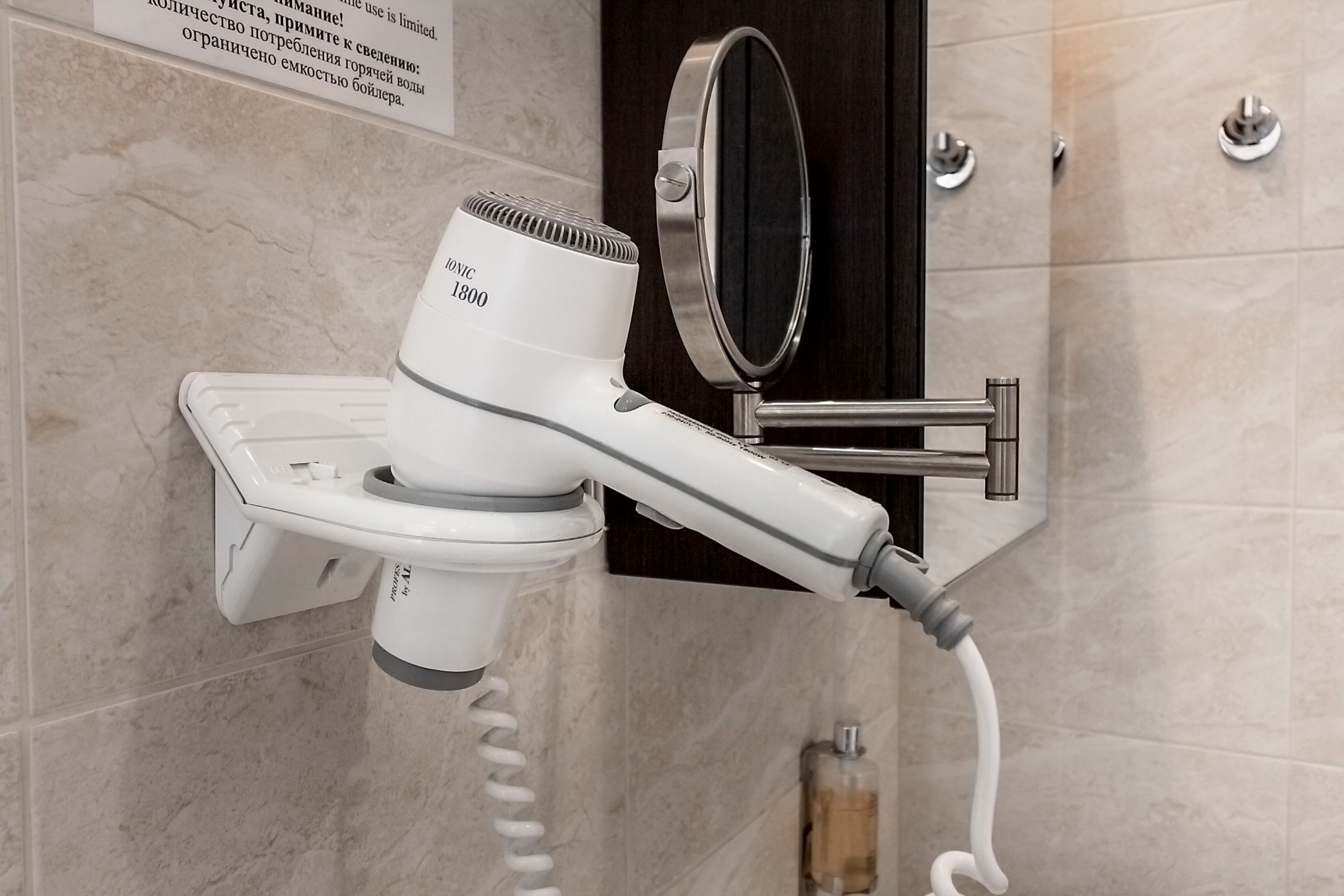 A hairdryer mounted on a wall in a bathroom with a mirror and a towel rack.