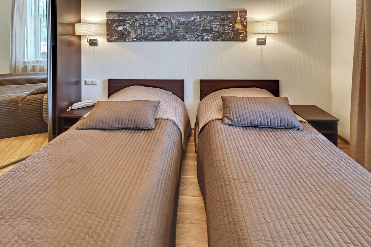 A hotel room with two beds, a cityscape artwork on the wall, and bedside lamps.