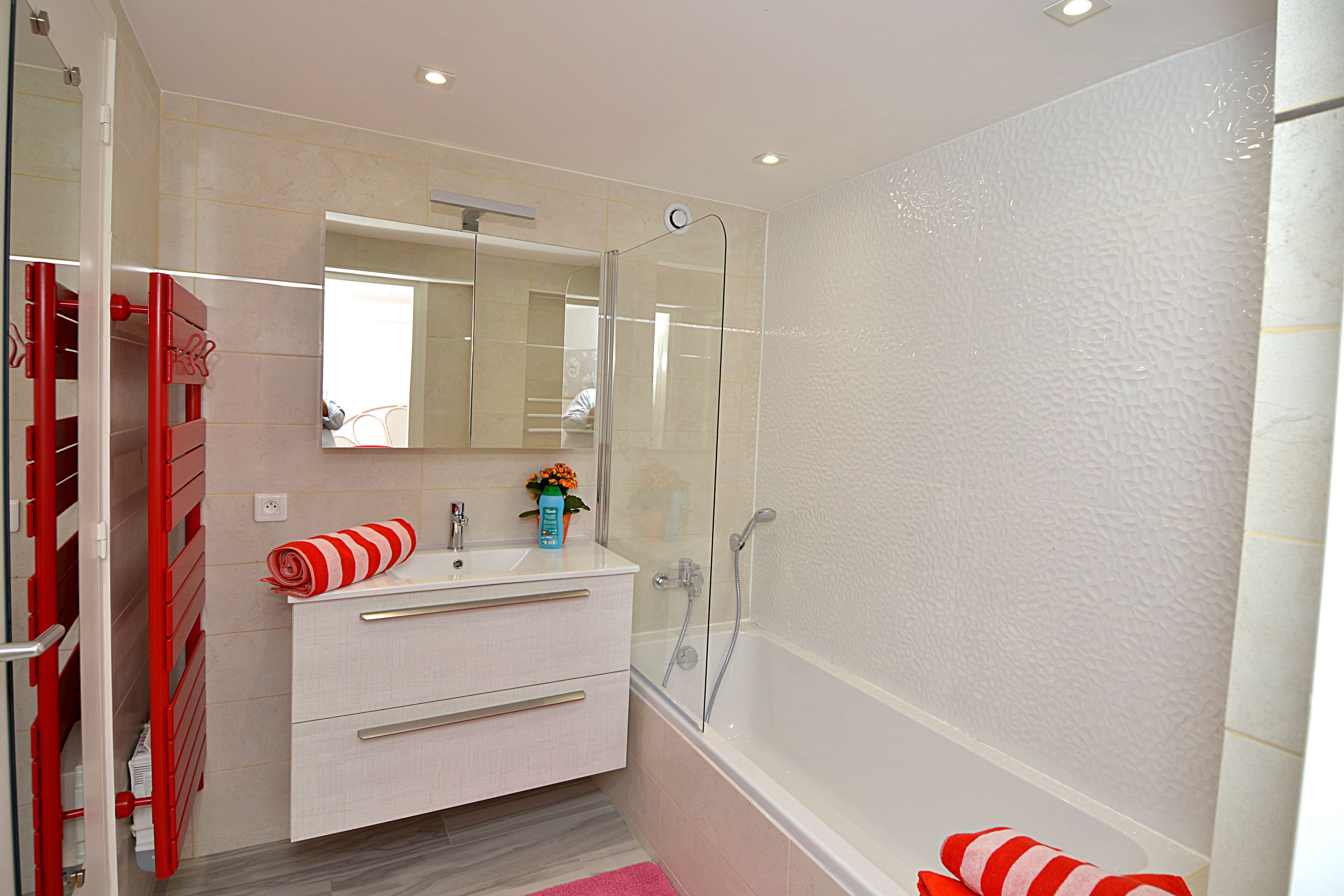 Un bagno con doccia vetrata, un mobile lavabo bianco con specchio e un porta asciugamani rosso.