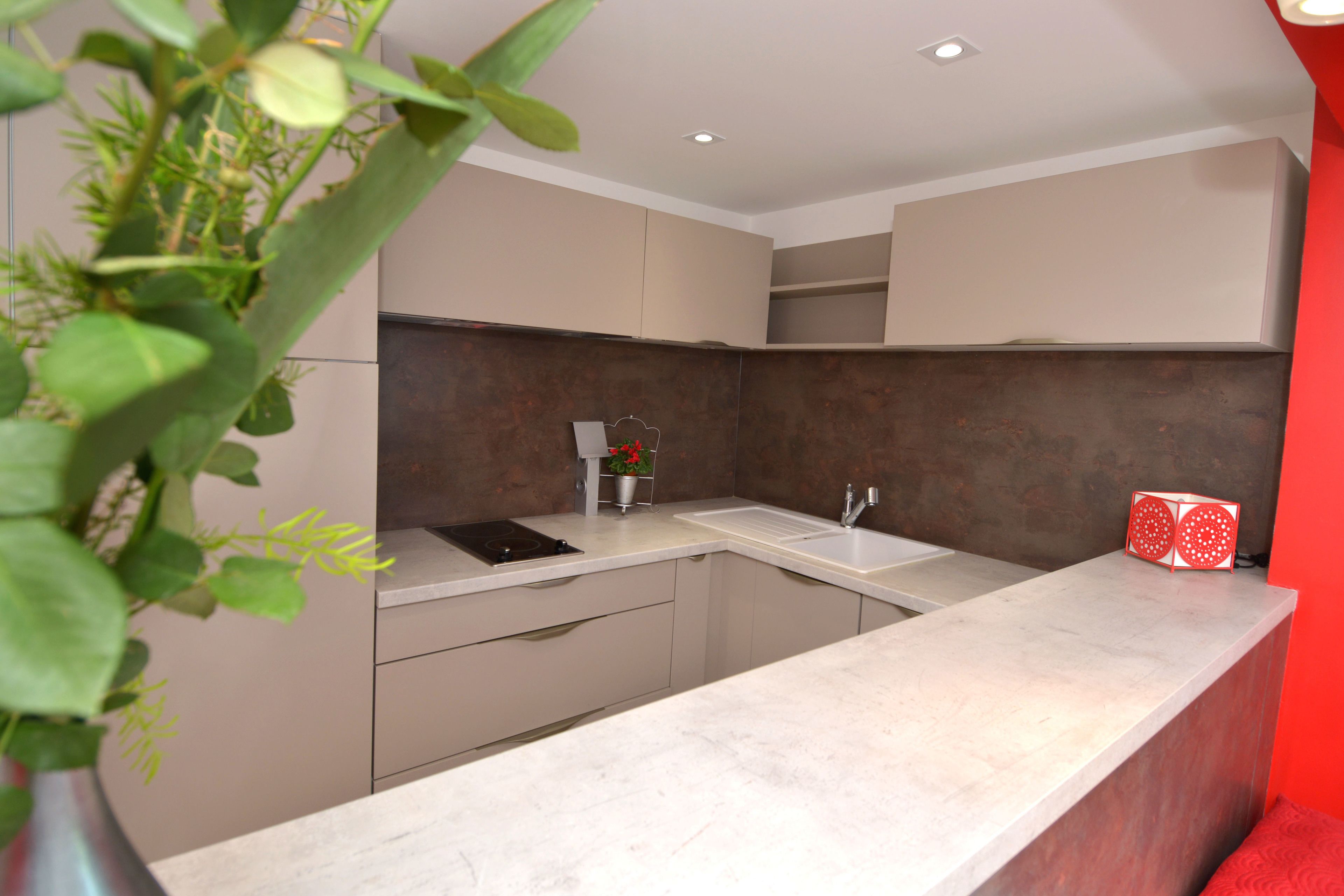A modern kitchen with a marble countertop, stainless steel appliances, and a red accent wall.