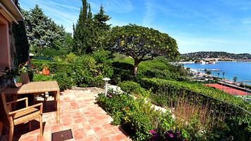 Un patio con mesa y sillas, vista al mar y un jardín exuberante.