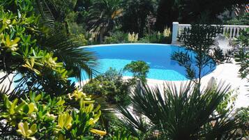 Una piscina circular rodeada de abundante vegetación y una valla blanca.