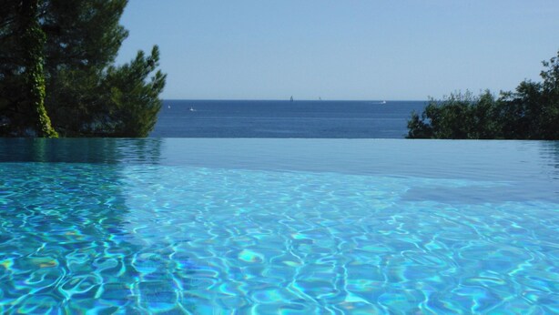 Vista chiara di una piscina con vista sull'oceano e alberi sullo sfondo.