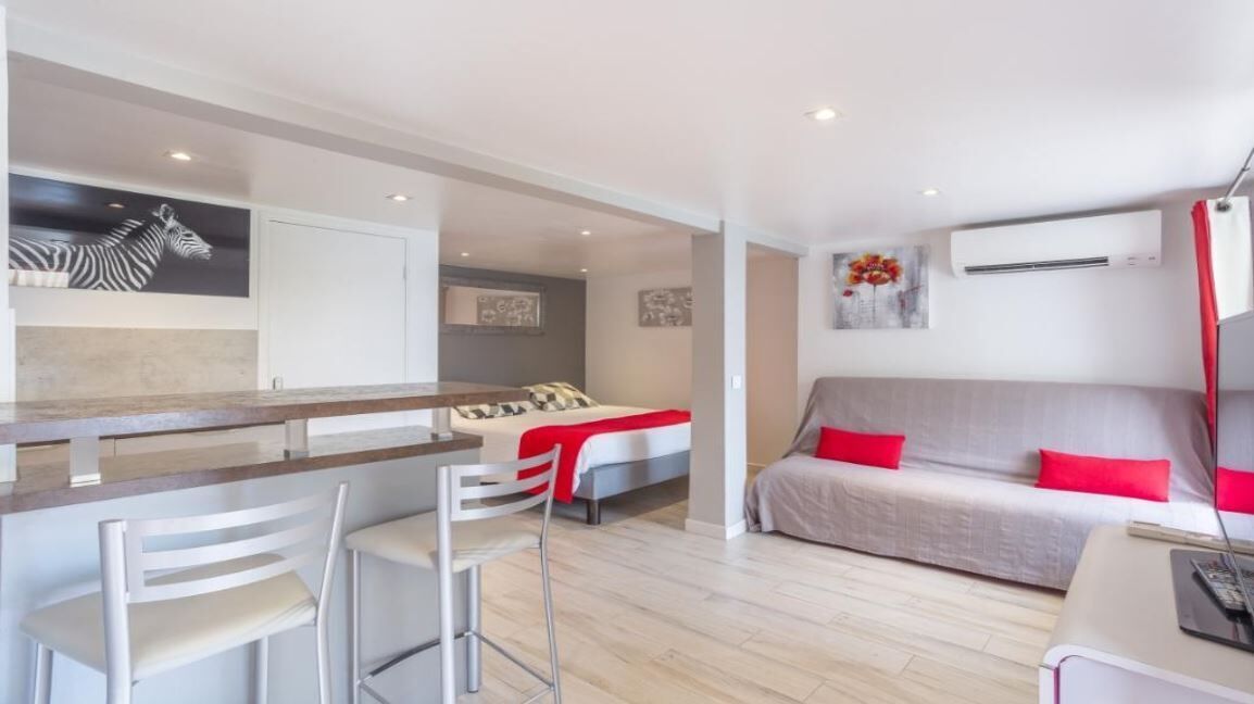 A modern hotel room with a kitchenette, a sofa, a bed, and a dining area.