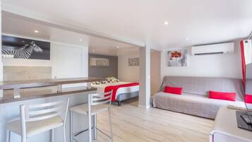 A modern hotel room with a kitchenette, a sofa, a bed, and a dining area.