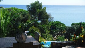 Un patio con una scultura in metallo, una sedia in vimini e un muro in pietra che si affaccia su una piscina e il mare.
