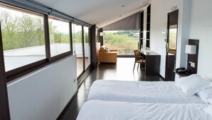 A modern hotel room with a large bed, a sofa, a desk, and a view of the outdoors. - Hotel Las Monteras (Villanueva del Rey)