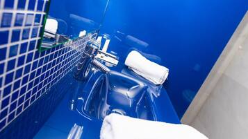 Un baño con pared de azulejos azules, un lavamanos cromado y una toalla blanca sobre el mostrador.