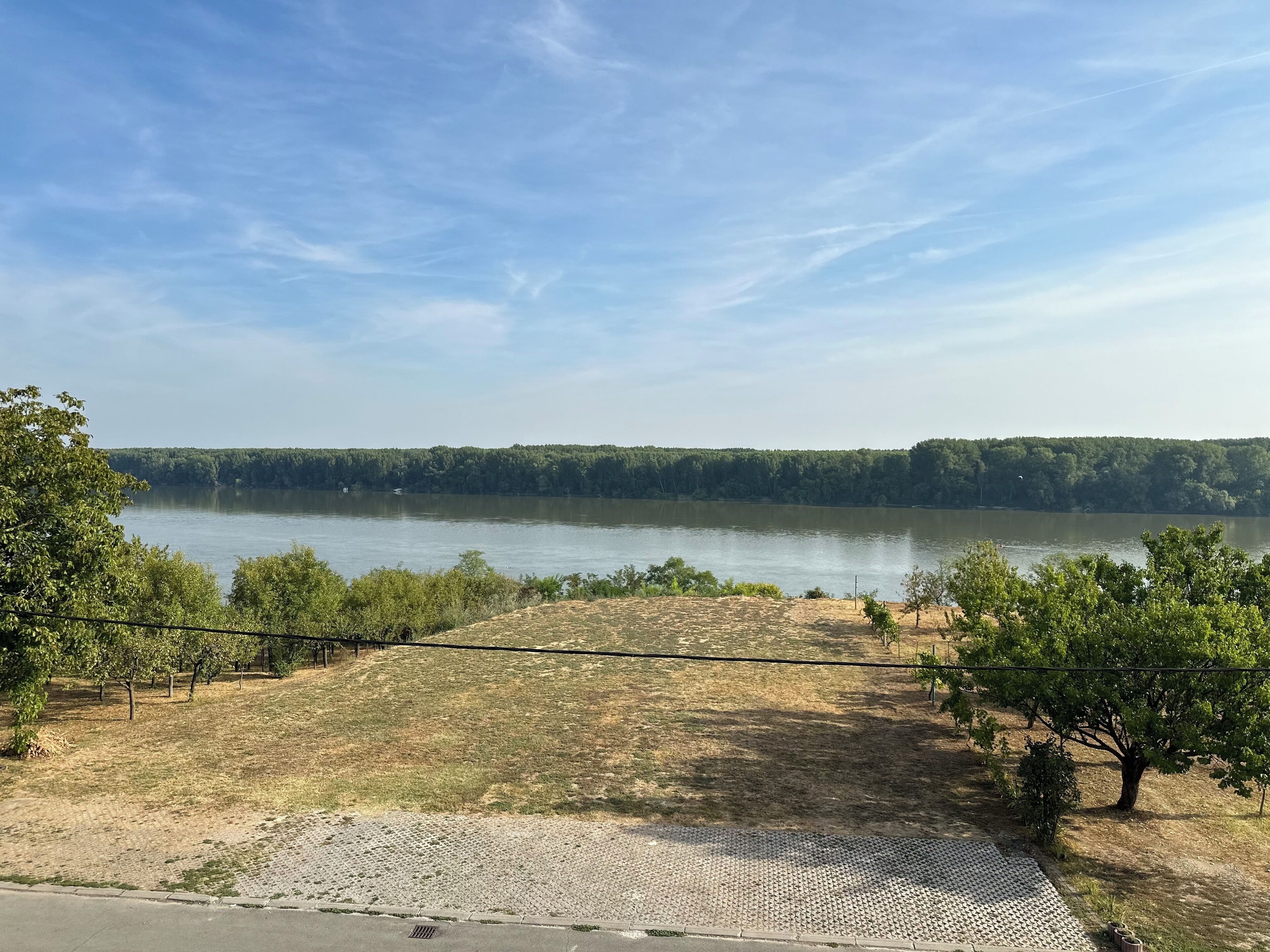 A view of a lake with a paved walkway and trees in the foreground.