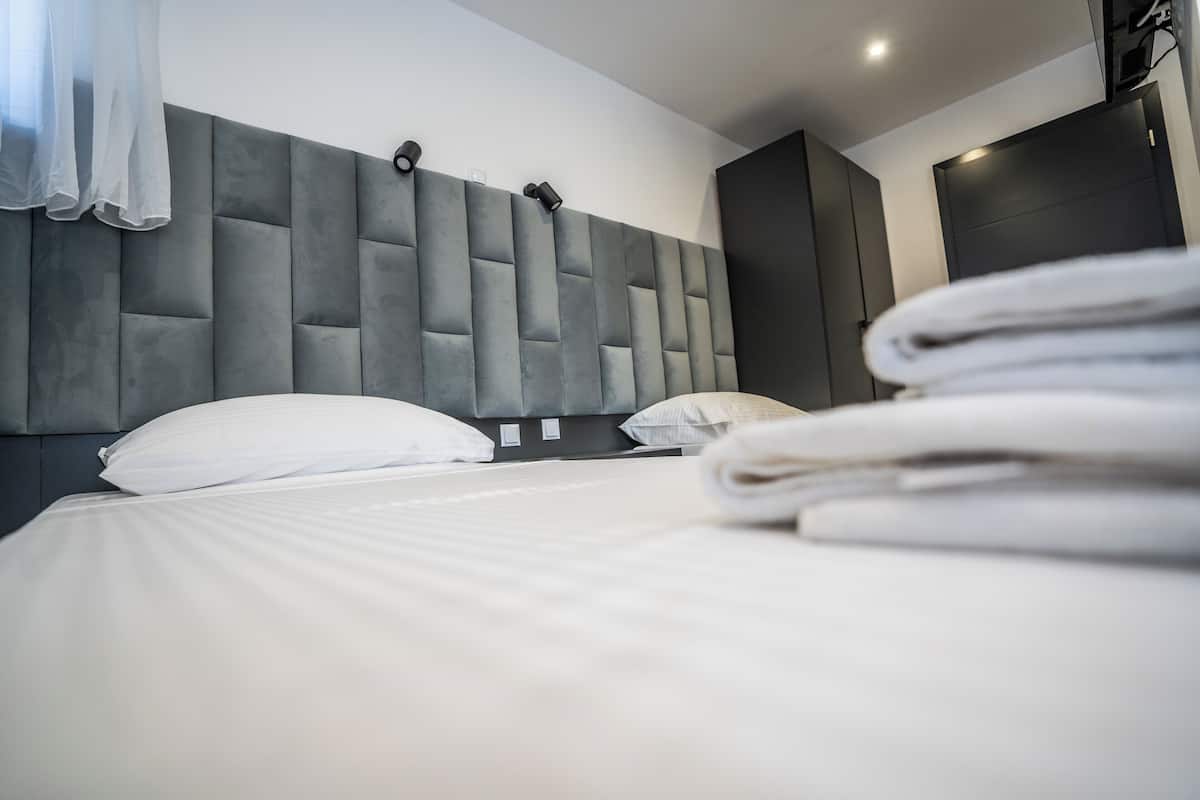 A hotel room with a large bed, a grey upholstered headboard, and a neatly made bed with white linens.