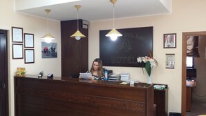 Un comptoir d'accueil d'hôtel avec un comptoir en bois, des certificats encadrés et un tableau noir sur lequel est écrit le mot « HÔTEL ».