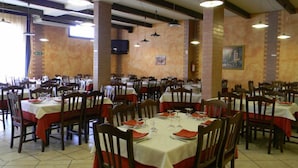 Un vaste espace dédié à la salle à manger, avec de nombreuses tables et chaises, de hauts plafonds avec des poutres apparentes et un téléviseur fixé au mur.
