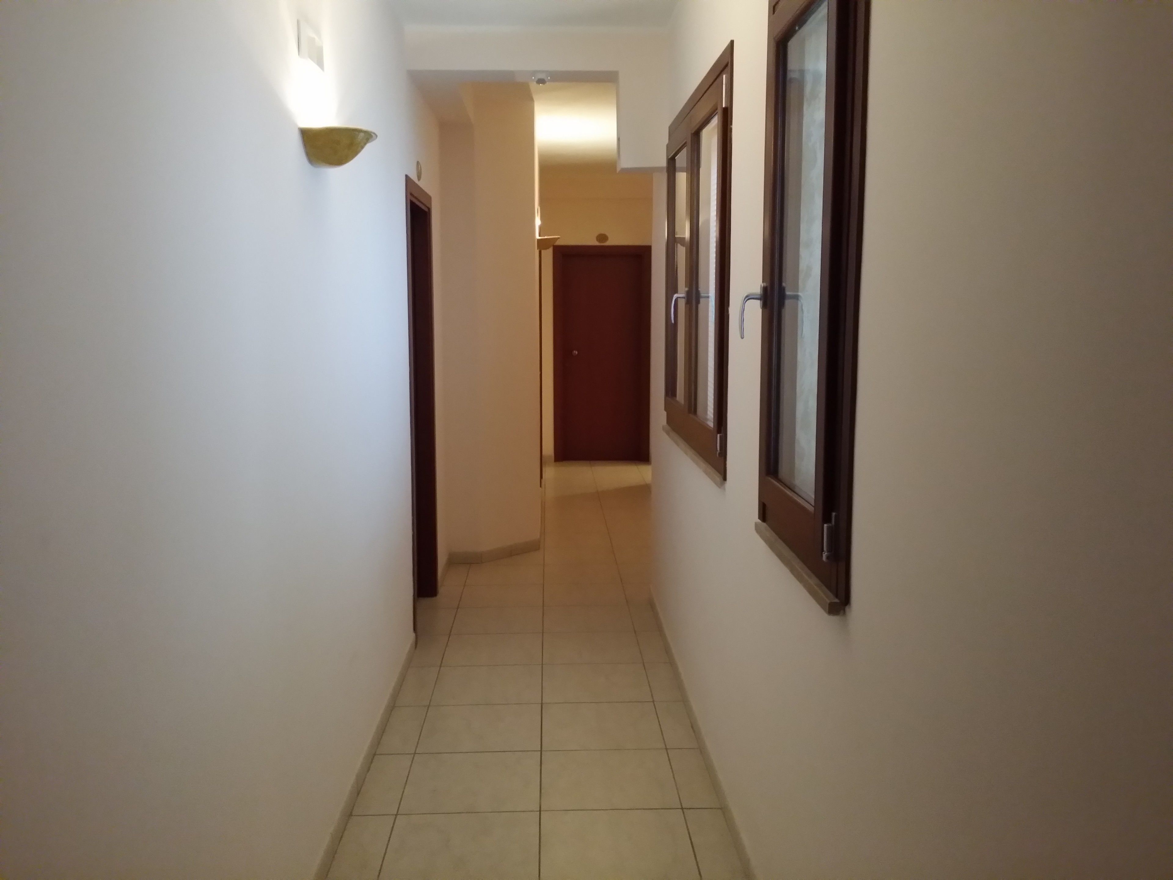 A hallway with tiled flooring, a light fixture on the left, and a door at the end.