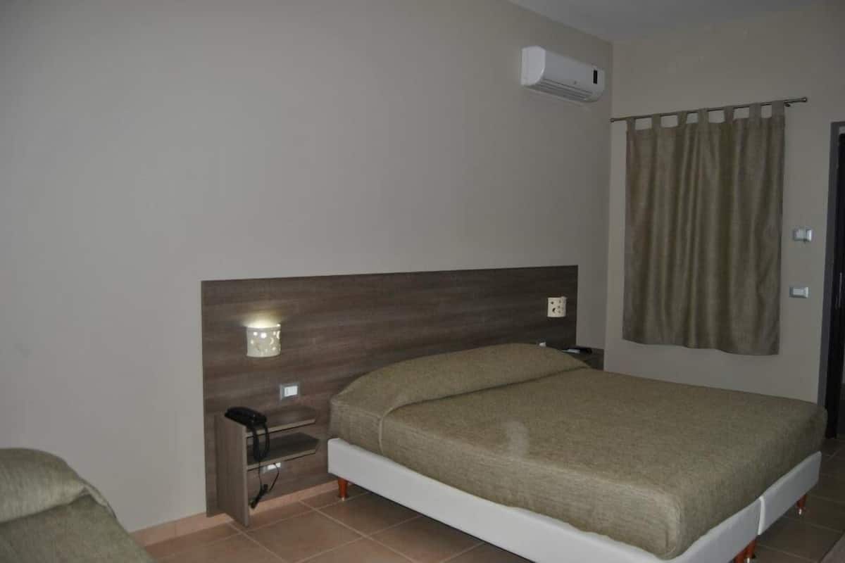 Een slaapkamer met een bed, nachtkastje, lamp en een airconditioning.