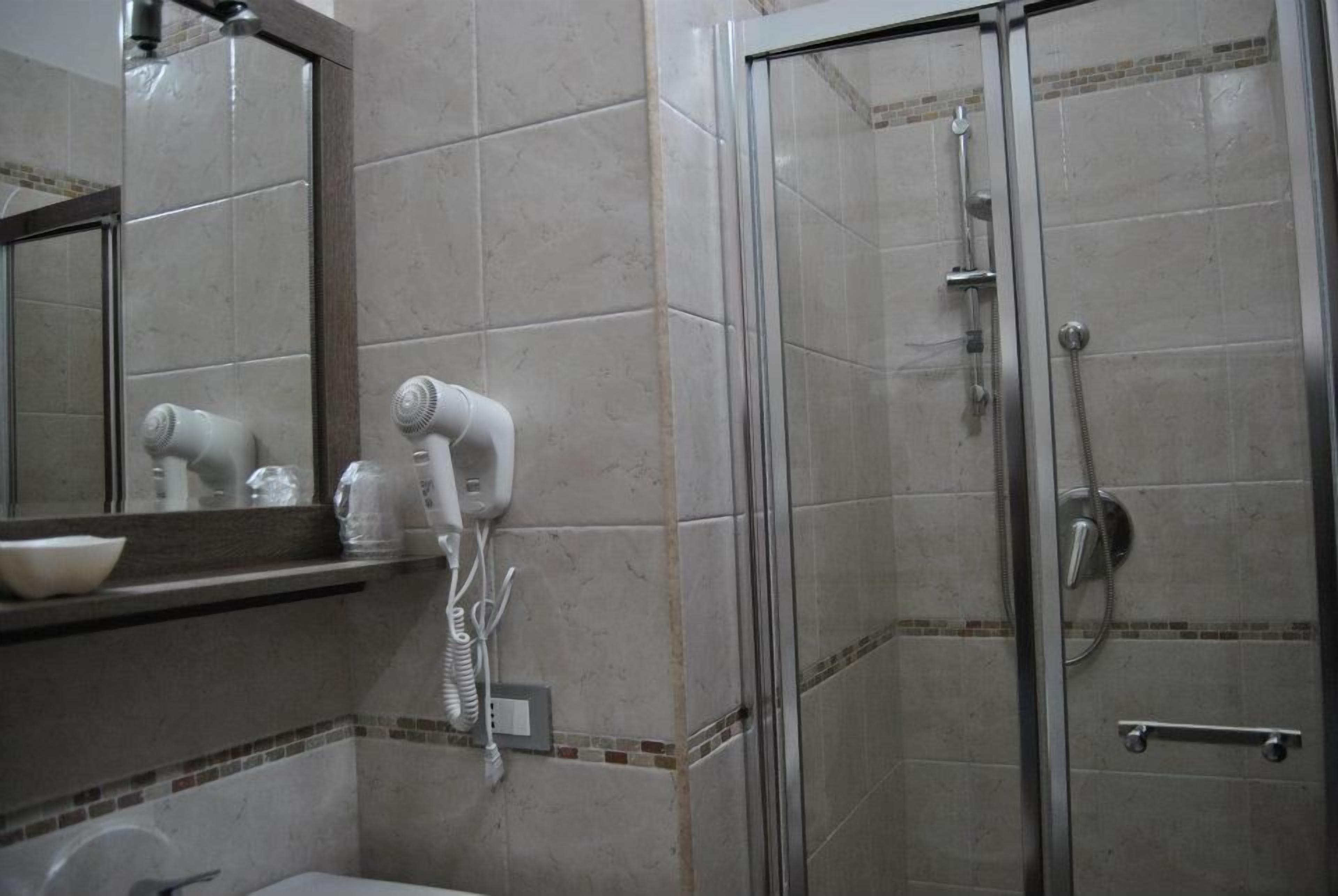 A bathroom with a glass shower enclosure, a hairdryer mounted on the wall, and a mirror above a sink with a bowl.
