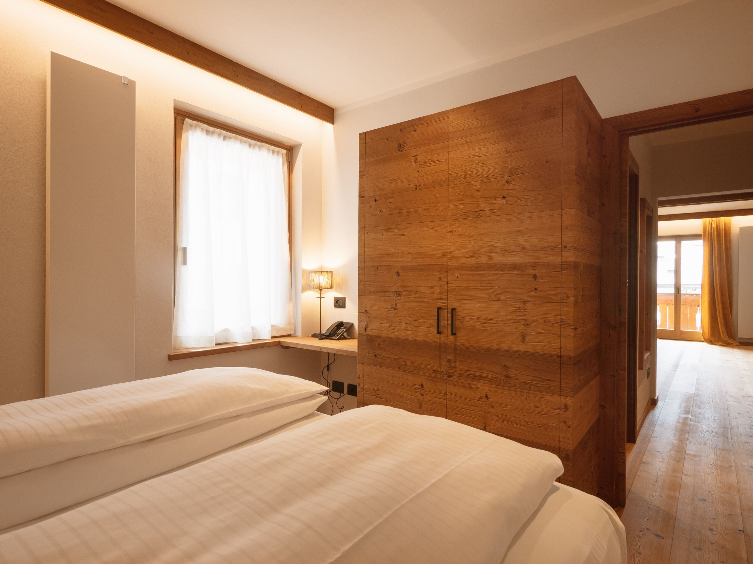 Ein Schlafzimmer mit zwei Betten, einem Holzschrank, einer Nachttischlampe und einem Fenster mit Vorhängen.