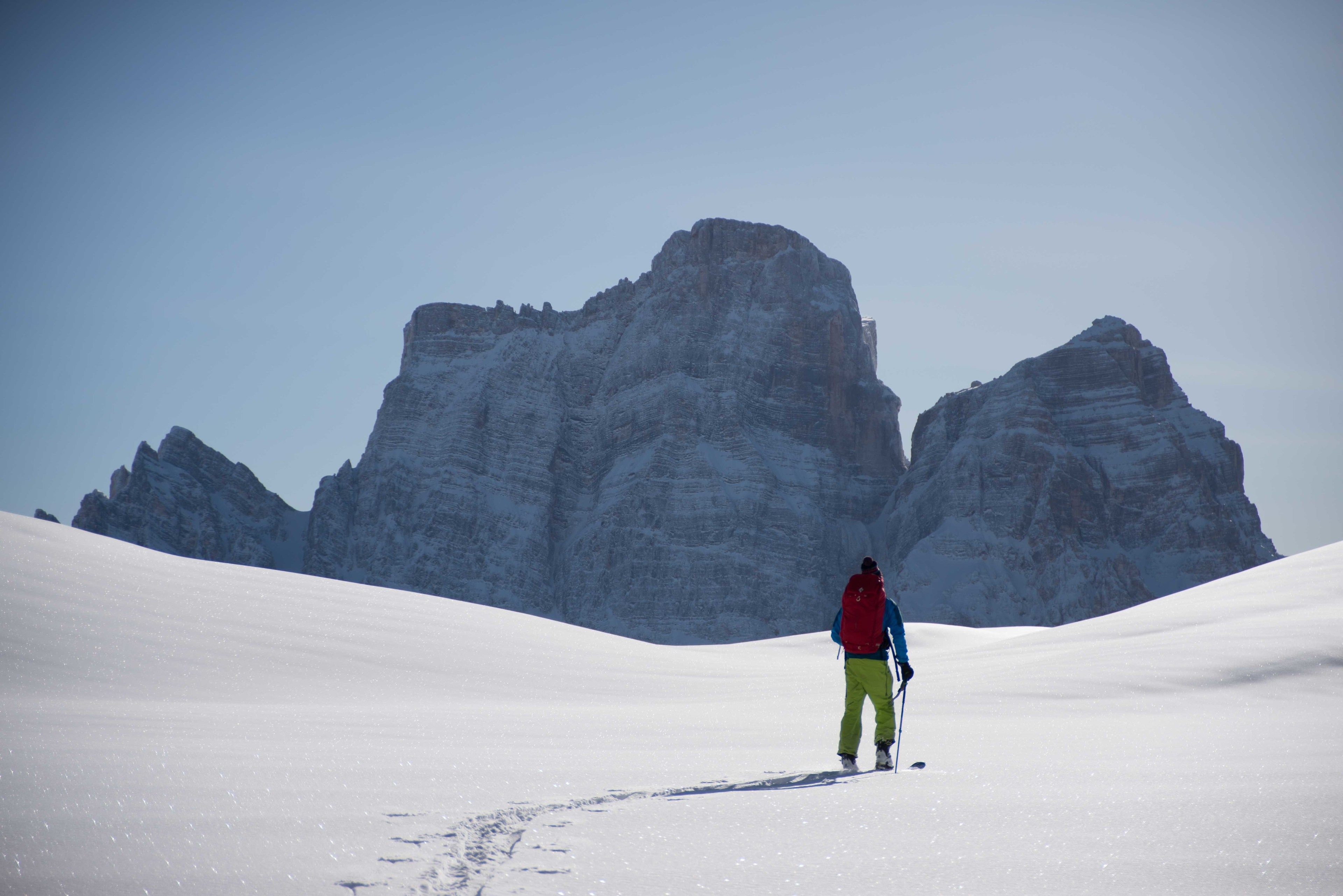 A person hiking on a snow-covered trail with a mountain in the background.