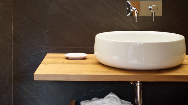 Un baño moderno con un lavamanos grande de color blanco, una encimera de madera y un espejo sobre el lavamanos.