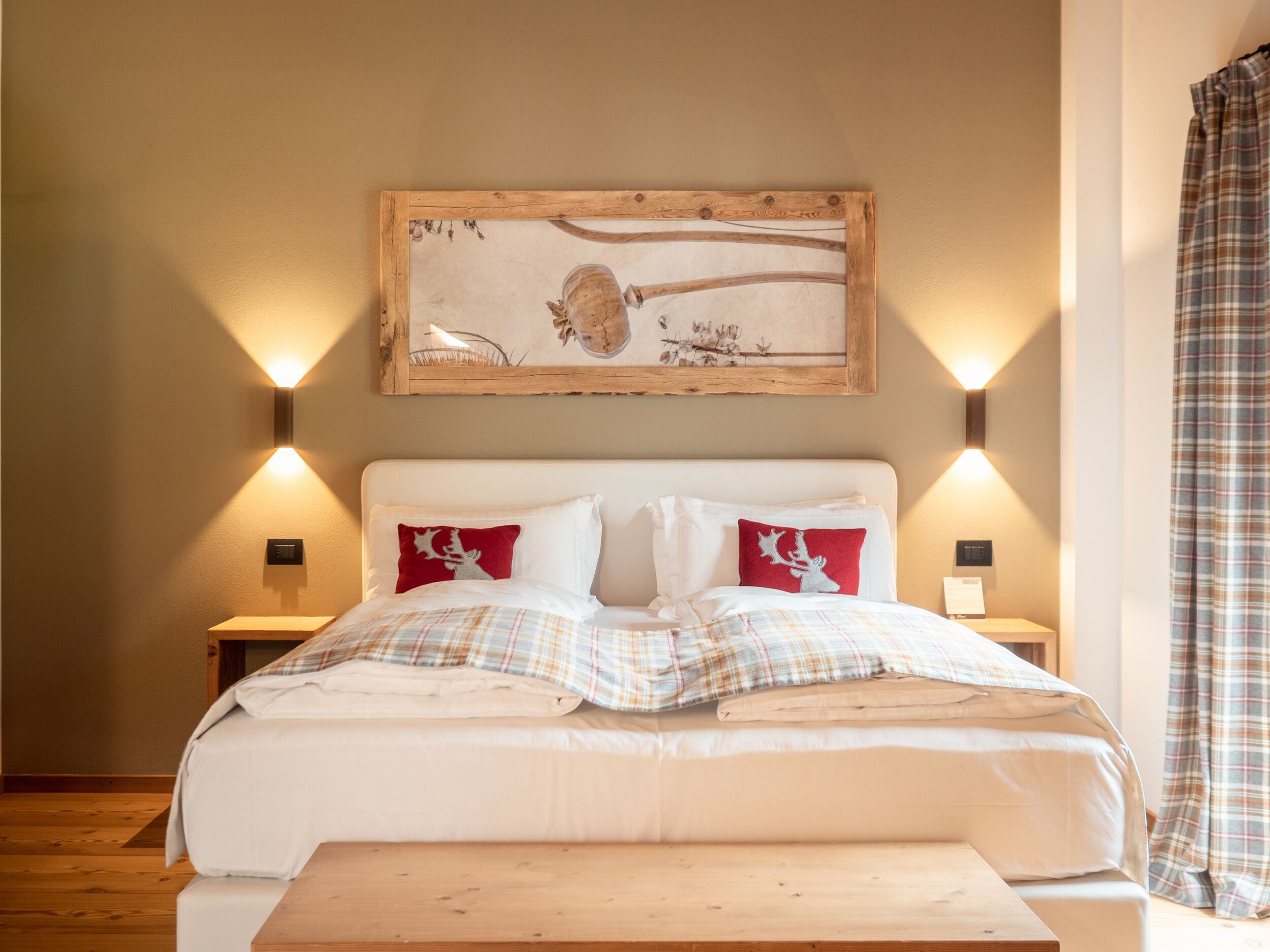 Quarto com uma cama grande, duas mesas de cabeceira, um banco de madeira e um quadro pendurado na parede.