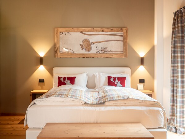 A bedroom with a large bed, two bedside tables, a wooden bench, and a wall-mounted painting.