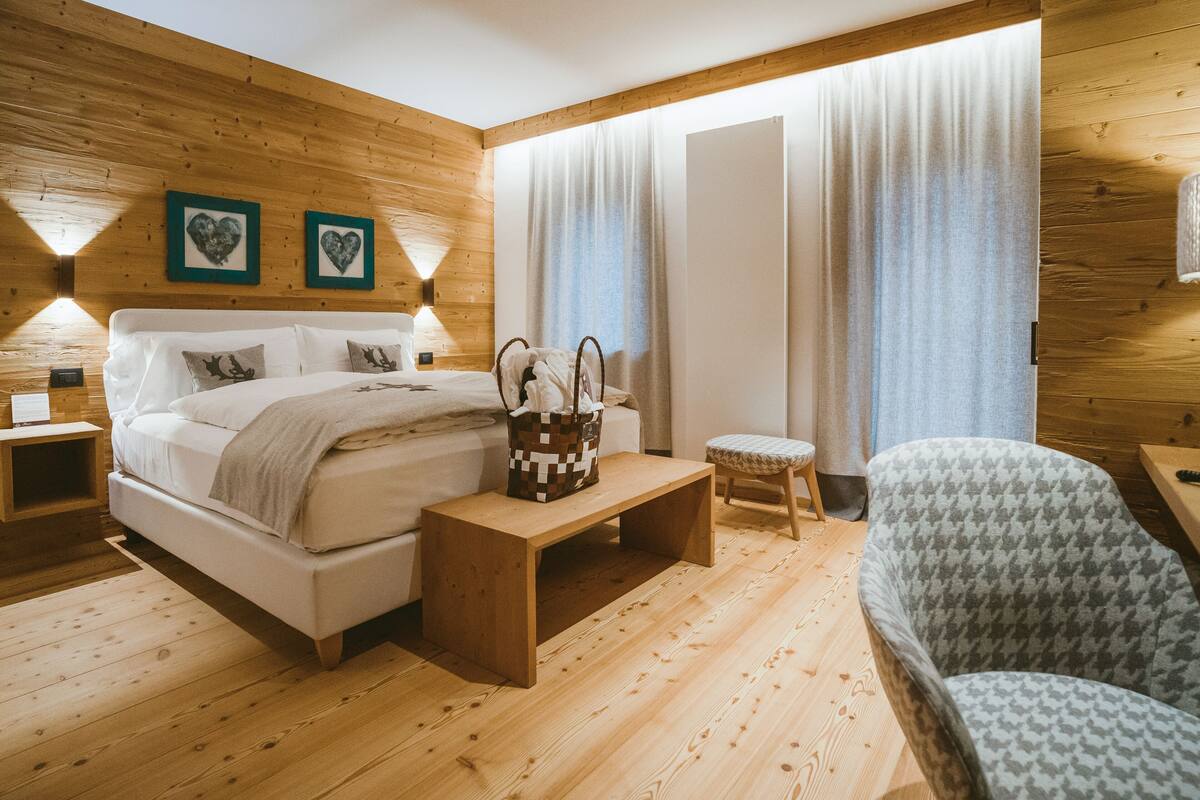 Una habitación con paneles de madera, una cama, mesitas de noche, un banco y un sillón estampado.