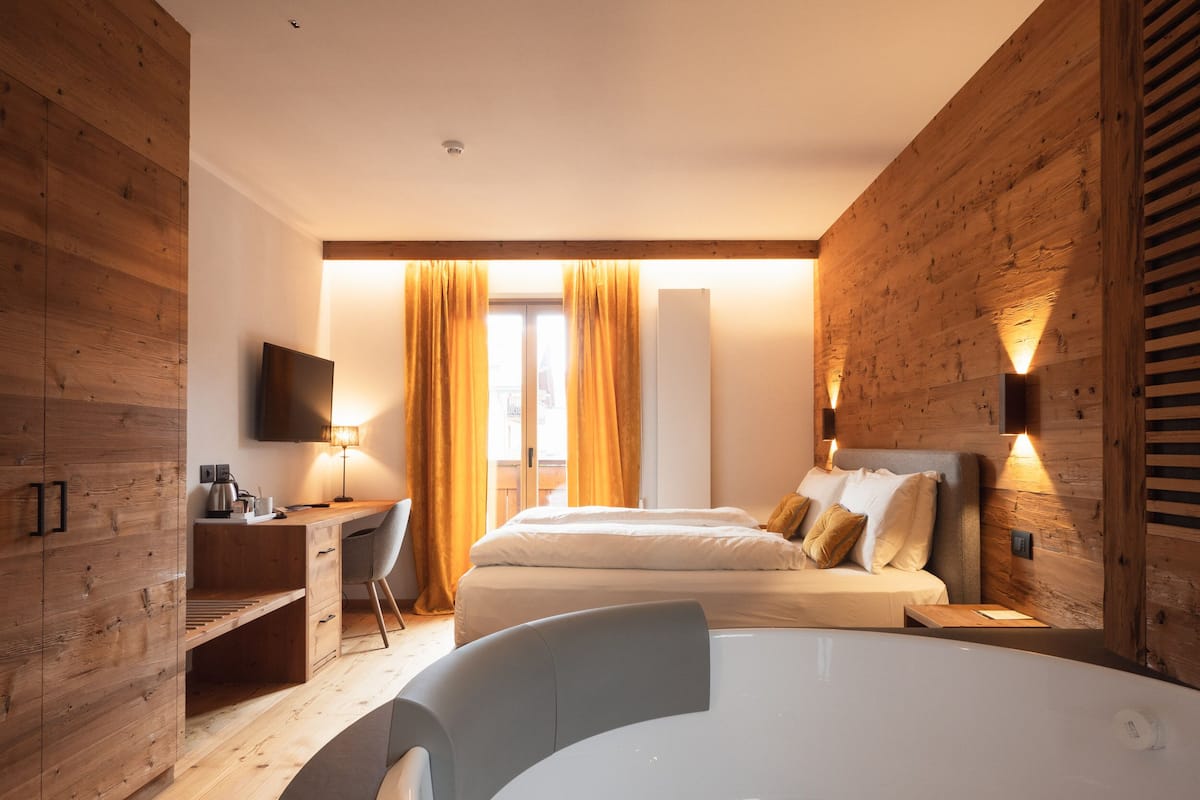 Una habitación de hotel moderna con paneles de madera, una cama, un escritorio, una silla, un televisor y una bañera.