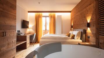 A modern hotel room with wooden paneling, a bed, a desk, a chair, a TV, and a bathtub.