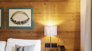 Habitación de hotel con pared de madera, cama con sábanas blancas, almohada gris con diseño de ciervo, escritorio pequeño con lámpara, teléfono y silla estampada.