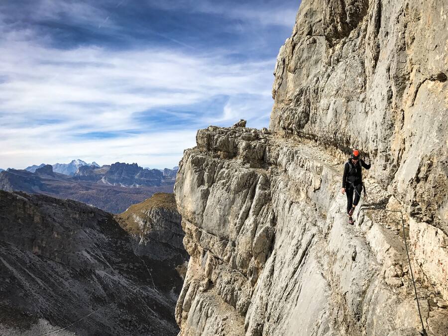 A person climbing a steep rock face with a mountainous landscape in the background.