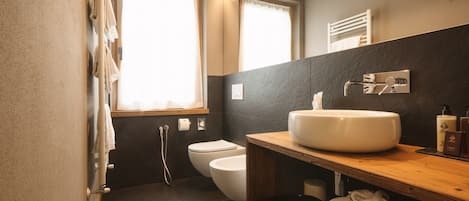 Un baño moderno con lavamanos grande, inodoro y ducha. Hay toallas y artículos de aseo en el mostrador.
