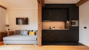 Ein modernes Wohnzimmer mit einer Couch, einem Flachbildfernseher, einer Küchenzeile inklusive Mikrowelle und Holzboden.