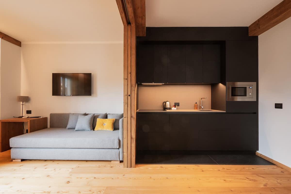 Un espacio habitable moderno con sofá, televisor de pantalla plana, zona de cocina con microondas y piso de madera.