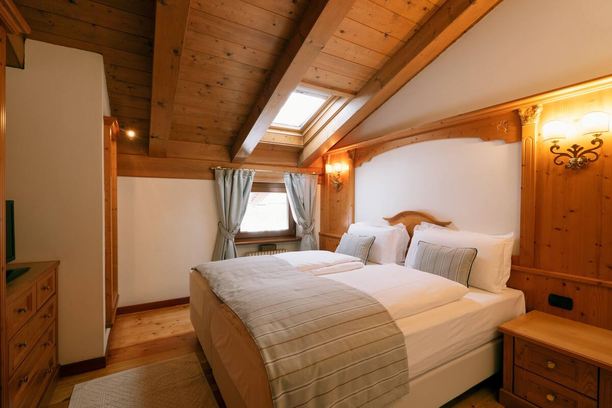 Un dormitorio de madera con una cama grande, dos mesitas de noche, un tocador y un tragaluz.