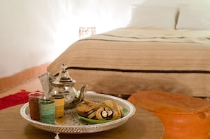 Een dienblad met koekjes en glazen op een houten tafel, een theepot, en een kussen op een bed.