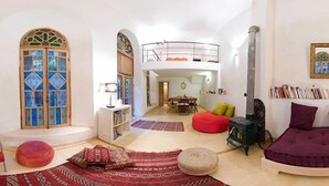 A cozy living room with a high ceiling, a fireplace, a red sofa, a red chair, and a bookshelf. - Riad La maison d'à côté (Meknes)