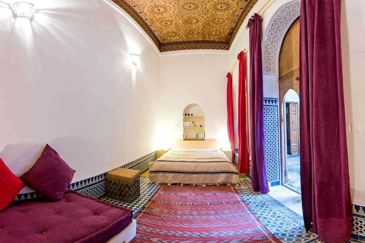 Una habitación con cama, sofá, alfombra estampada y vistas al exterior.